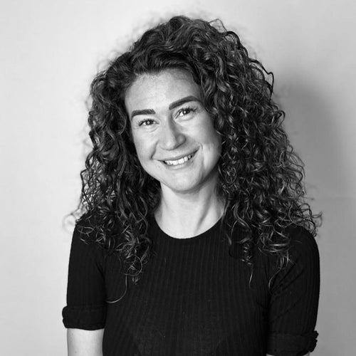 Smiling woman with curly hair in a black top, photographed in black and white against a plain background.