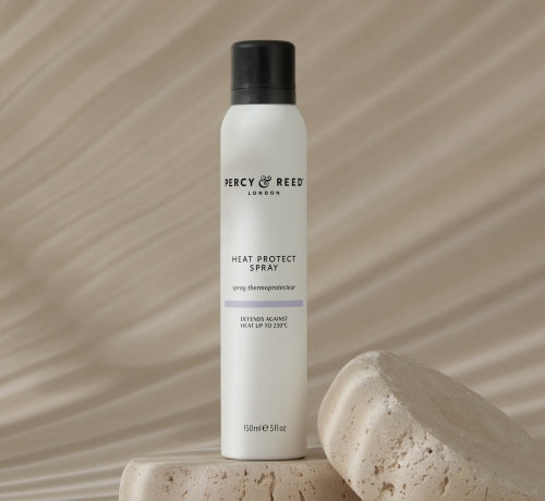 A white bottle of Percy & Reed Heat Protect Spray on stone slabs, with a beige wavy background.