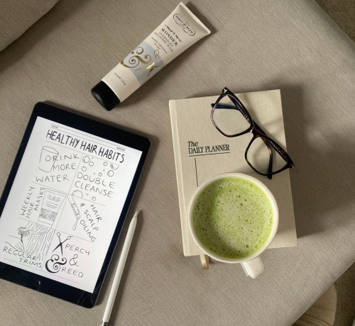 Tablet showing hair care tips, planner, glasses, lotion, pen, and green tea on a beige surface.