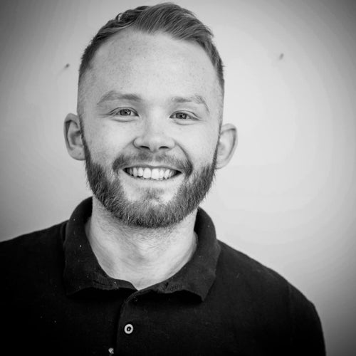 Smiling man with a beard and short hair, wearing a dark polo shirt, in black and white.