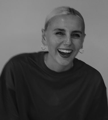 Smiling person with short hair and hoop earrings, wearing a dark shirt against a plain background.